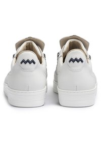 Sneakers bianchi in pelle caratterizzati da una texture liscia, punta arrotondata e accenti zigzag neri a contrasto sul tallone. Design minimalista.