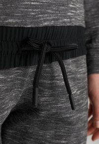 Gros plan d'un vêtement en tricot gris avec une ceinture élastique noire nouée par un cordon noir à l'avant.