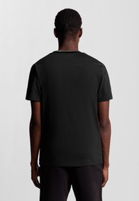 T-shirt in cotone nero con scollo rotondo, maniche corte e una texture liscia. La vista posteriore mostra un design pulito e una vestibilità rilassata.