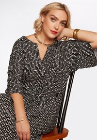 Abito a righe in bianco e nero con scollatura a V e maniche larghe. Presenta una vita definita e un design geometrico. Accompagnato da gioielli dorati.