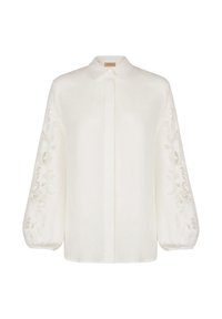 Witte linnen blouse met lange balloonmouwen met gedetailleerd borduurwerk aan de zijkanten en een klassieke kraag. Voorzijde met knopen.