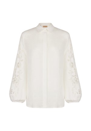 Biała lniana koszula z długimi, balonowymi rękawami ozdobionymi misterną haftowaną dekoracją po bokach oraz klasycznym kołnierzykiem. Zapinana na guziki z przodu.