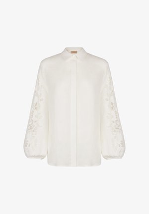 Biała lniana koszula z długimi, balonowymi rękawami ozdobionymi misterną haftowaną dekoracją po bokach oraz klasycznym kołnierzykiem. Zapinana na guziki z przodu.