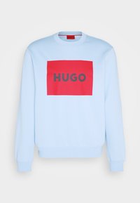 Sweat-shirt bleu clair à col ras du cou, avec un grand graphisme rectangulaire rouge portant le texte "HUGO" en gris. Texture de tissu doux.