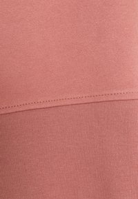 Tejido rosa claro con una textura suave y un patrón acanalado en la parte inferior. Los detalles de las costuras corren horizontalmente a lo largo de la prenda.