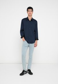 Cămașă albastru închis cu mâneci lungi și design cu nasturi, manșete negre contrastante, asortată cu blugi bleu și adidași negri.