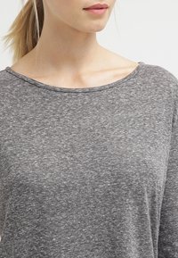 Maglietta grigia a maniche lunghe con scollo ampio e tessuto morbido e texture. Cuciture visibili e vestibilità rilassata.