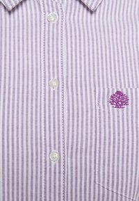 Chemise à boutons rayée violet et blanche, avec une poche ornée d'un design d'arbre brodé et un col classique. Tissu texturé.