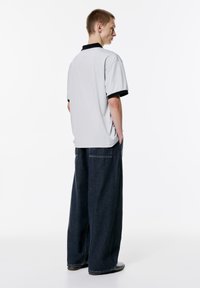 Lysegrå polo-shirt med en sort krave, parret med løstsiddende mørkeblå jeans. Outfittet har en afslappet og rummelig pasform.