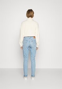 Világos krémszínű, oversize pulóver hosszú ujjal, világoskék, magas derekú farmernadrággal párosítva. Figyelemre méltó Levi's márkajelzés a hátsó részen.