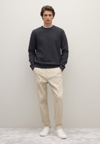 Dunkelgrauer, strukturierter Pullover mit Rundhalsausschnitt, kombiniert mit beigen Chinos und weißen Turnschuhen, für ein entspanntes, legeres Outfit.