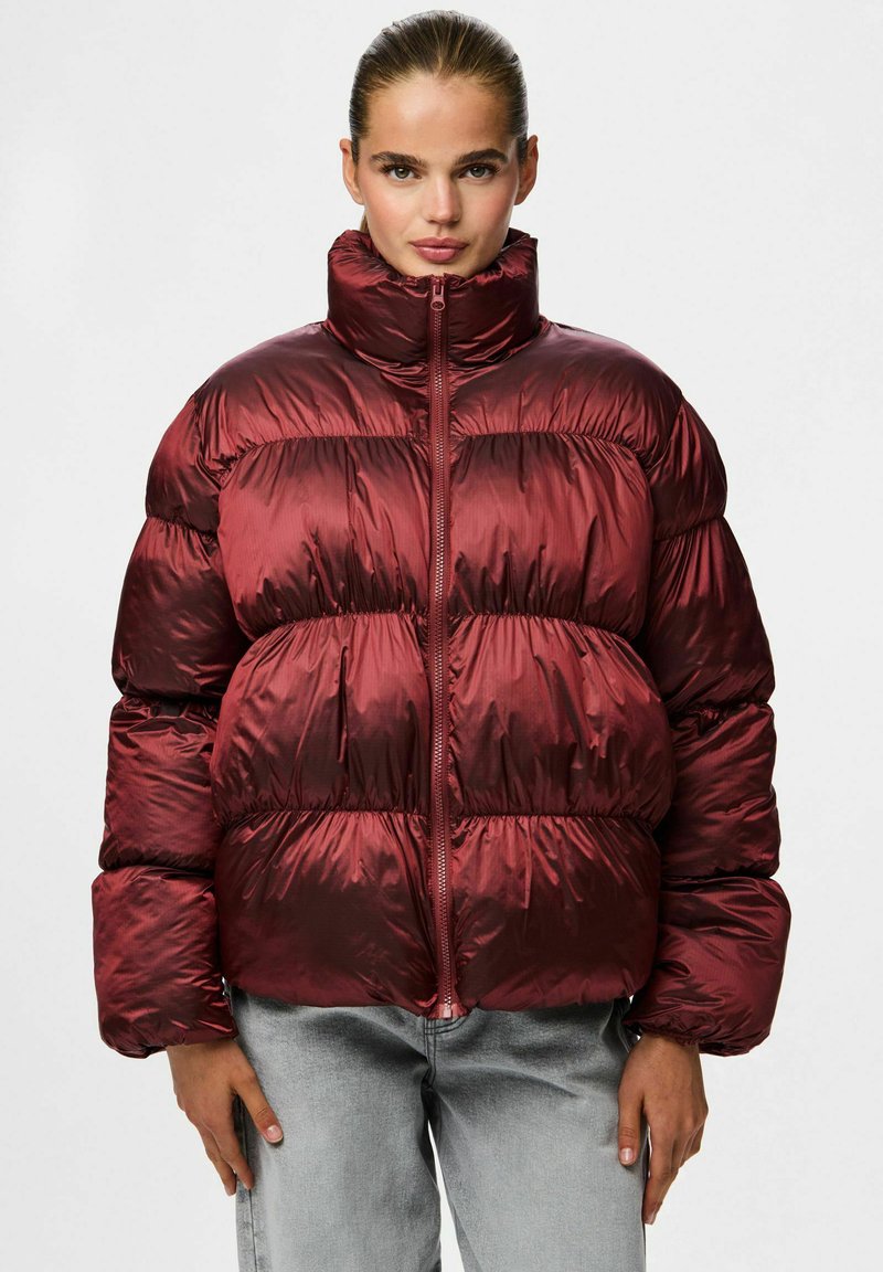 Bordo pūkinė striukė su aukštu apykakle, raukšlėta tekstūra, priekiniu užtrauktuku ir didelė siluetas, derinama su šviesiai pilkais džinsais.