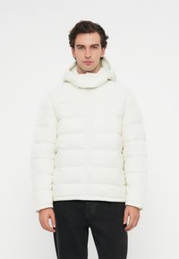 Λευκή φουσκωτή ζακέτα με κουκούλα, με οριζόντιες ραφές, κλείσιμο με φερμουάρ και πλαινές τσέπες. Υφασμάτινη επιφάνεια με λεία υφή.