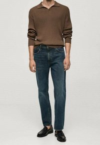Brązowa, prążkowana koszulka polo z długim rękawem, proste ciemnoniebieskie dżinsy, czarne buty eleganckie. Prosty design, teksturowana tkanina i dopasowany krój.