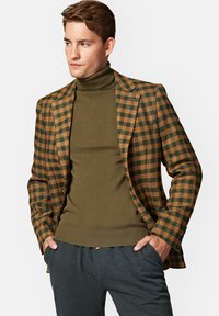 Brązowo-zielona marynarka w kratę z fakturowanej tkaniny, połączona z oliwkowym golfem. Ciemnoszare spodnie dopełniają stylizację.
