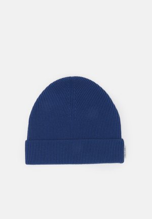 Bonnet bleu en tricot côtelé avec revers plié et petite étiquette de marque blanche sur le côté, présenté sur un fond clair uniforme.