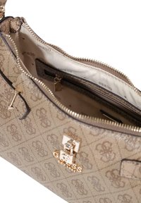 Bolso beige con un patrón de monograma, detalles dorados y cierre superior con cremallera. El interior cuenta con un forro de tela y un pequeño bolsillo.