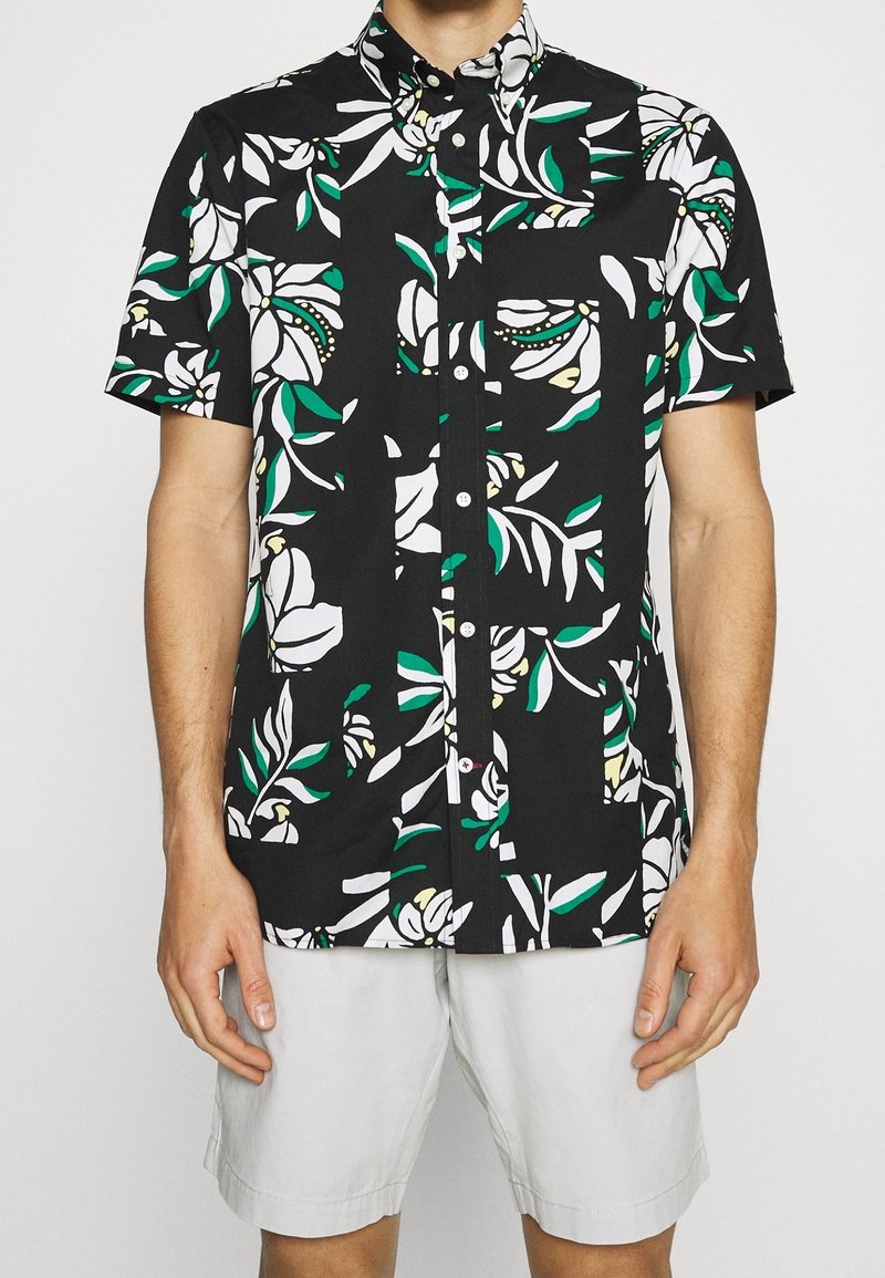 Chemise à manches courtes en coton noir avec motifs floraux blancs et feuilles vertes, dotée d'un col boutonné et d'une fermeture à boutons sur le devant.