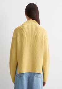 Gelber Strickpullover mit gerippter Textur, weiten Ärmeln und hohem Kragen. Mit einem entspannten Schnitt und einem überschnittenen Schulterdesign.