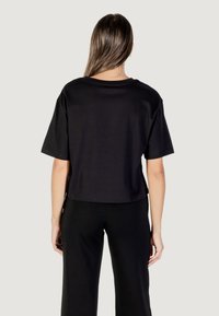 Camiseta negra corta de algodón suave con mangas cortas. Diseño simple, cuello redondo y líneas limpias, combinada con pantalones negros a juego.