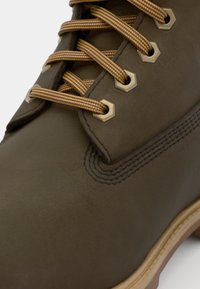 Boot din piele maro cu ochiuri hexagonale, sireturi galbene și maro, cusături întărite și o talpă bej contrastantă.