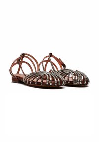 Scarpe sandalo con una tomaia in pelle marrone, caratterizzate da dettagli metallici argentati e una suola piatta, che mostrano una punta aperta e un motivo a reticolo.