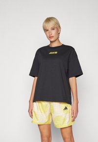 Must musta T-särk lühikeste varrukatega ja kollase logoga. Kombineeritud kollaste lühikesed püksid triibulise mustriga ja Adidas logo. 