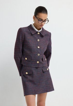 Tweed jacket in dark purple with red accents and gold buttons, paired with a matching skirt. Features large collar and two front pockets.