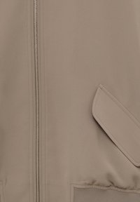 Chaqueta bomber beige con una cremallera plateada, que presenta una textura suave, bolsillos laterales y puños elásticos para un ajuste ceñido.