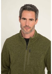 Pullover in felpa di colore verde scuro con una finitura testurizzata. Presenta un colletto alto e due tasche sul petto con zip per lo stoccaggio.