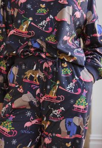 Pyjamasett i mjukt tyg med en mörkblå bakgrund och färgglada djurillustrationer, inklusive elefanter och flamingos på kälkar.