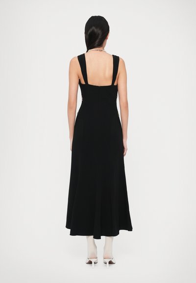 Juoda, be rankovių suknelė su plačiomis petnešėlėmis, aptempta liemene ir laisvai krentančia sijono dalimi. Nugaroje yra užtrauktukas, o šonuose - detalių.