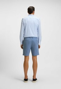 Light blue striped long-sleeve shirt with buttoned cuffs, paired with solid blue shorts. Visible rear pockets and casual black shoes.