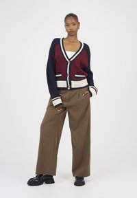 Wpleciony kardigan w kolorze burgundowym i granatowym, z dekoltem w kształcie V, zapięciem na guziki i prążkowanymi mankietami. Połączony z beżowymi spodniami o wysokim stanie i czarnymi butami.