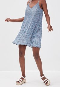 Robe à imprimé floral bleue avec un col en V et des bretelles réglables. Tissu léger plissé créant une silhouette fluide. Sandales compensées blanches.