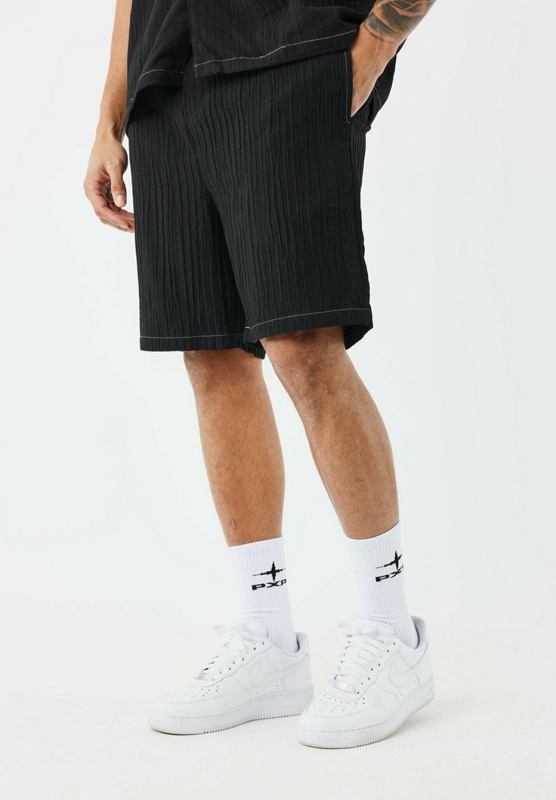 Shorts negros de canalé con dobladillos enrollados, con bolsillos laterales. Combinados con zapatillas Nike Air Force 1 blancas y calcetines con logo blancos.