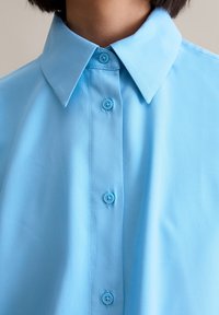 Sky blue short-sleeve shirt with a classic collar, featuring six button closures and a smooth, lightweight fabric.