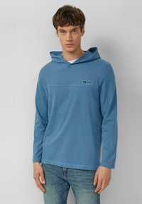 Bluza z długim rękawem i kapturem w jasnoniebieskim kolorze o gładkiej fakturze, z logo na przedniej części i luźnym krojem.