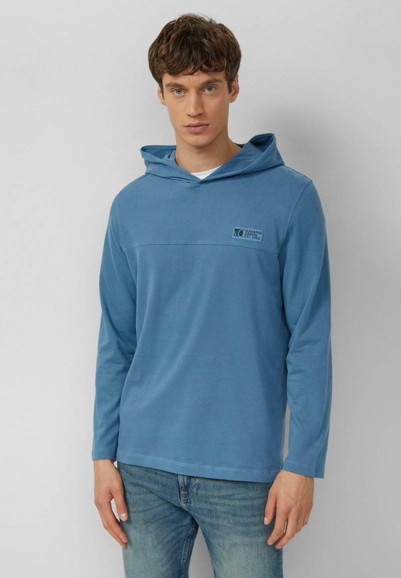 Bluza z długim rękawem i kapturem w jasnoniebieskim kolorze o gładkiej fakturze, z logo na przedniej części i luźnym krojem.