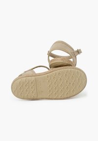 Sandalias de esparto beige con suela de yute trenzado, parte superior de tela, correa ajustable en el tobillo y suela de goma texturizada con un patrón ondulado.