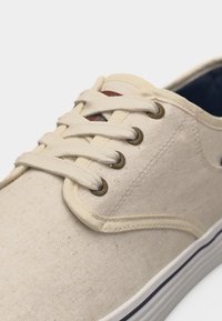 Μπεζ αθλητικό πάνινο παπούτσι casual με λευκά κορδόνια, μεταλλικά μηχανήματα και λευκή καουτσούκ σόλα με λεπτή μαύρη ρίγα.