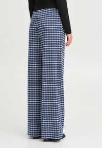 Weite Hosen im blau-weißen Karomuster. Aus weichem Stoff mit fließendem Design gefertigt. Mit hohem Taillenbund und langem Schnitt.
