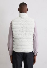 Leichte weiße Steppweste mit horizontalen Steppnähten, hohem Kragen und Seitentaschen, getragen über einem gestreiften Langarmshirt und dunkler Hose.