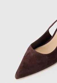 Kengät tummanruskeasta mokasta, teräväkärkiset slingback-mallit, joissa on vaaleanbeige sisäpohja, vaaleanharmaalla taustalla.