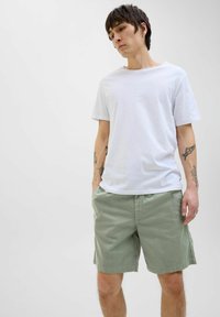 Camiseta blanca de manga corta combinada con pantalones cortos de algodón verde claro. Los pantalones cortos cuentan con bolsillos laterales y un ajuste relajado.