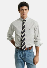 Hvidternet button-down skjorte med optrukne ærmer, parret med et stribet slips i blå, gul og rød. Båret med lyseblå denimjeans og et brunt bælte.