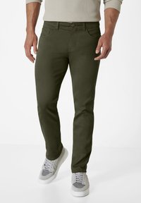 Olive green, slim-fit pants with a smooth texture, five pockets, and a button closure, paired with gray sneakers.