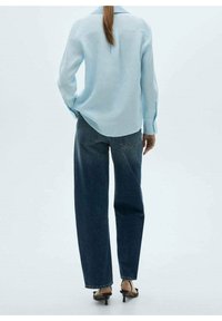 Chemise boutonnière à manches longues bleu clair, coupe décontractée, associée à un jean droit taille haute bleu foncé et des sandales à talons noires.