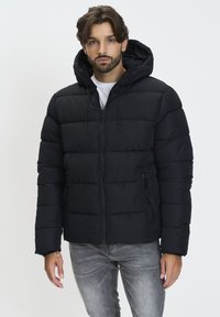Jachetă puffer neagră cu glugă și fermoar frontal. Prezintă un model matlasat orizontal și două buzunare laterale. Este asortată cu blugi gri.