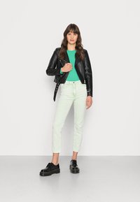 Jaqueta de cabedal preta de motard sobre uma camisa verde com canelados, combinada com jeans verde menta claro e sapatos plataformas pretos com costura amarela.